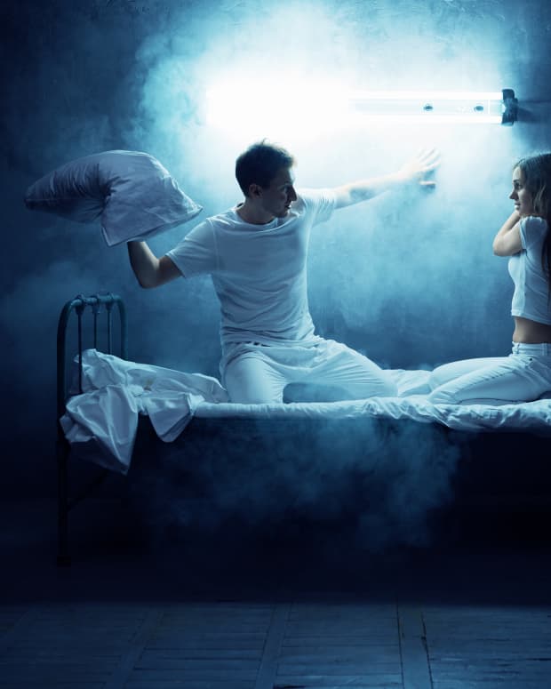 a couple in a dramatic pillow fight with dramatic lighting in a dark room
