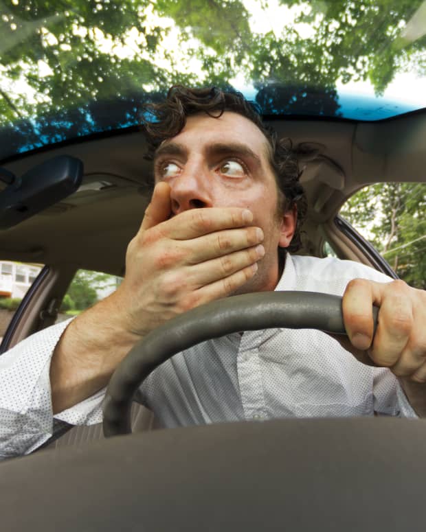 a distorted image of a driver behind the wheel of a car, his hand over his mouth in shock, his eyes wide.