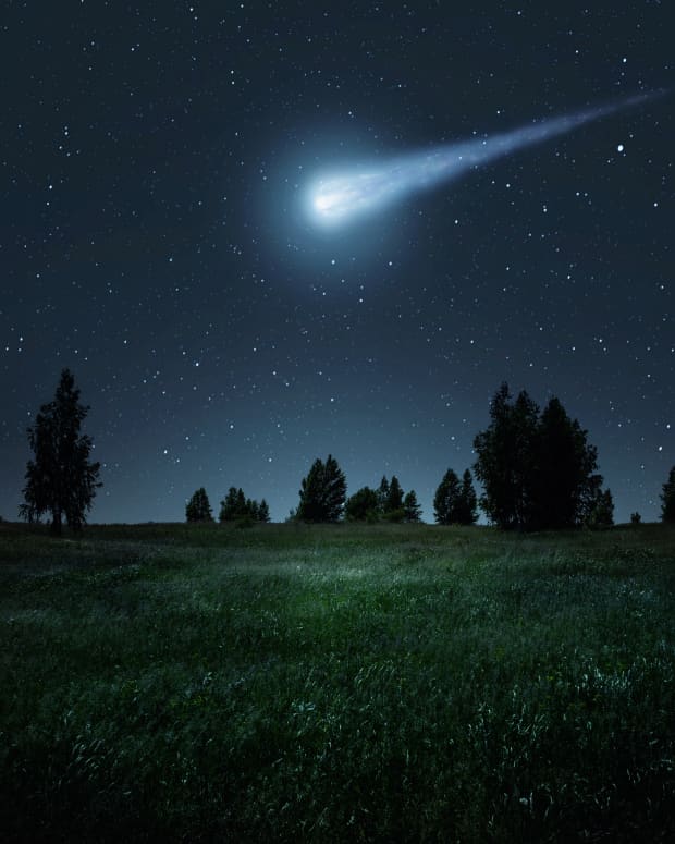 A meteor lights up a night sky over a wooded field