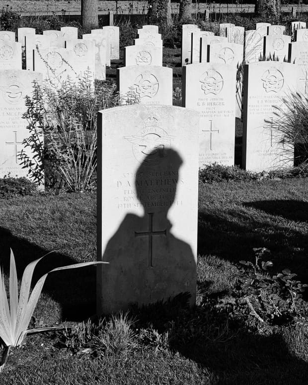 a black and white image of grave headstones. The one in the foreground features a shadow of a man's silhouette