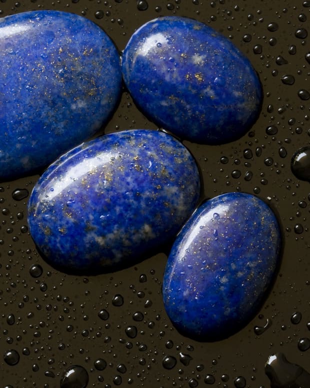 Several polished lapis lazuli stones on a black background, beaded with water. They look like tiny, oblong Earths in space
