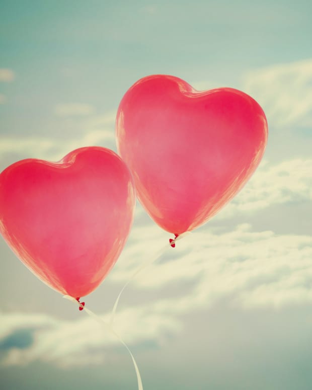 Red heart-shaped balloons against a blue, cloud filled sky.
