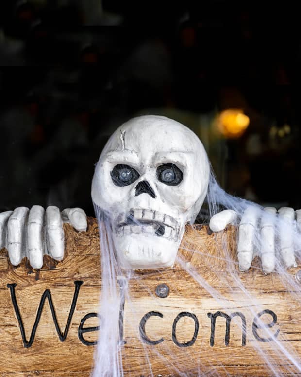 A spooky Halloween "Welcome sign" decor, with a skeleton covered in cobwebs peeking up over the top of the wooden sign.