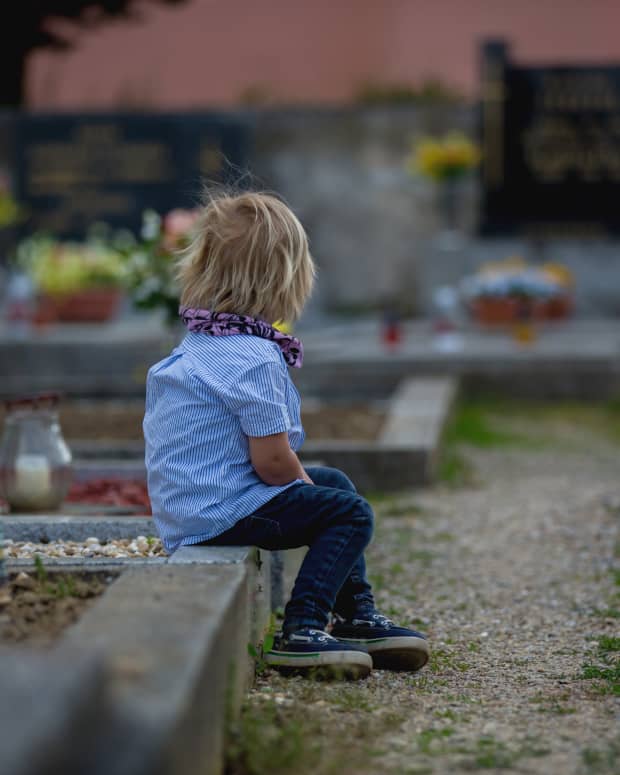 A child sits in a graveyard facing away from the camera