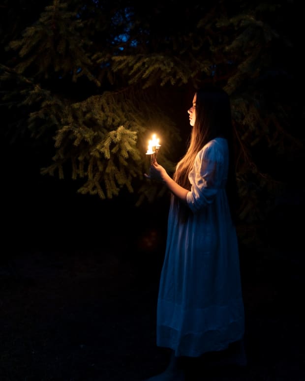 a girl in a nightdress holds a candle in a dark wood