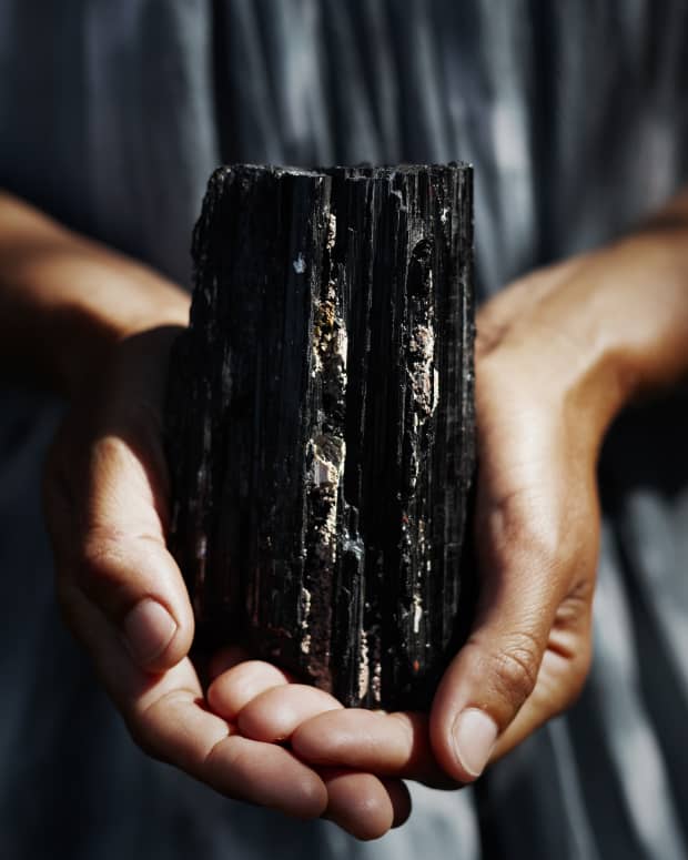 close up on a woman's hands holding a large, jagged chunk of black tourmaline
