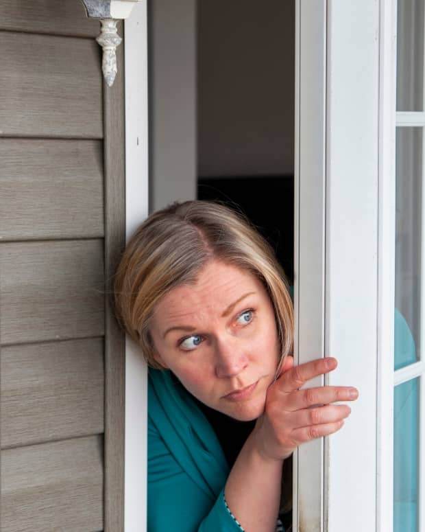a woman peeks out of her front door, looking frightened.
