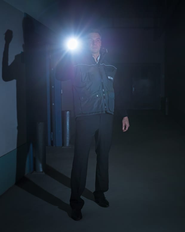 a security guard with a flashlight in a dark and creepy hallway