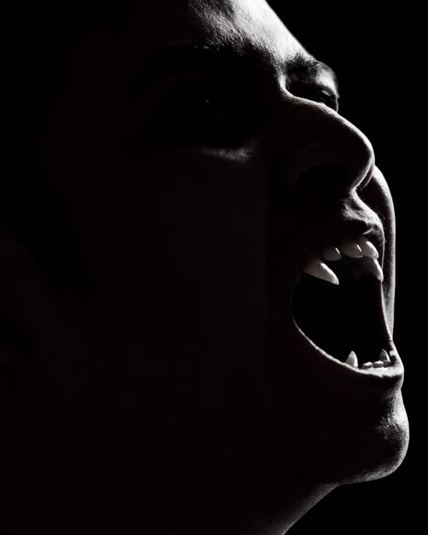 a shadowy black and white picture of a vampire, mouth open, ready to bite.