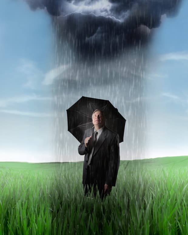 a man in a suit is standing under an umbrella in a green field where a dark rainstorm is pouring on ONLY him and everywhere else is sunny.
