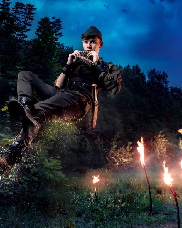 peter pan plays a pan flute and hovers over a wilderness lit by torchlight.