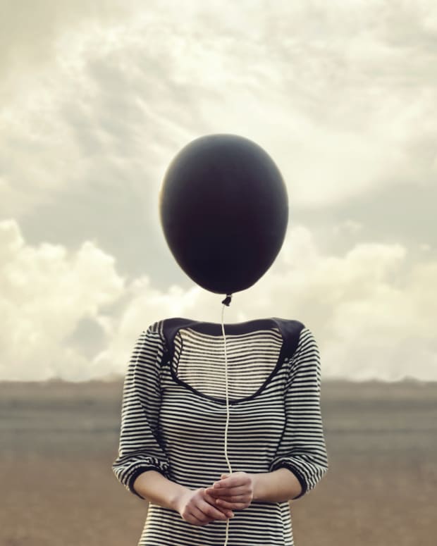 a headless woman stands in a field holding a black balloon where her face should be.
