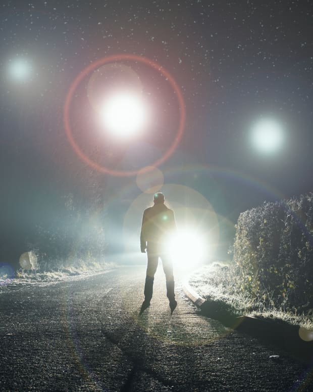 a man stands on a road at night. Strange lights shimmer above him in the sky