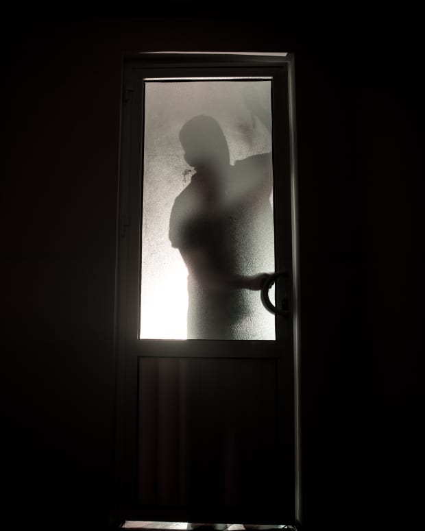 a man's shadow lurks behind a glass door