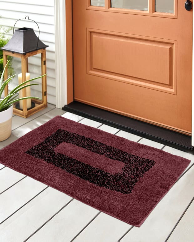 a red doormat in front of a neat front door and porch.