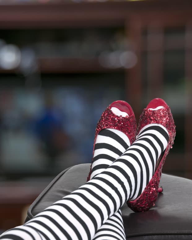 a close up on striped-tights covered legs wearing ruby slippers a'la the Wicked Witch of the West, but with the feet up on a coffee table like she's watching TV.