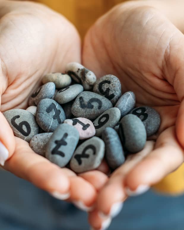a woman cups a handful of gray polished river stones with numbers written on them in black ink.