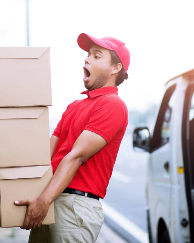 a delivery man in a red t shirt and hat looks shocked as he carries boxes