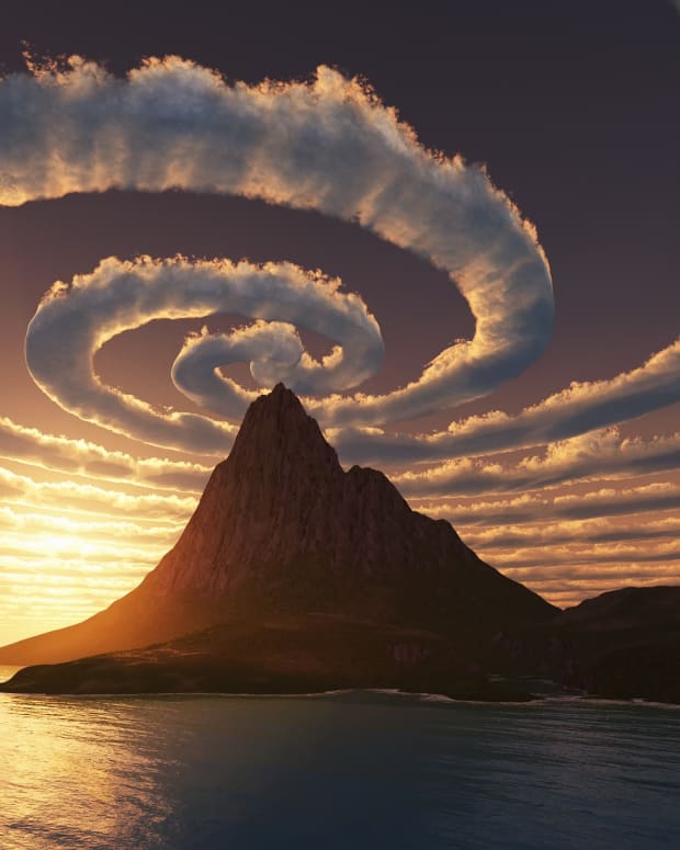 clouds making a vast spiral over the peak of a mountain over water at sunset
