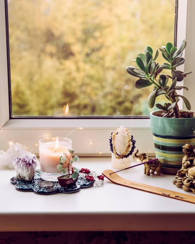 a money tree, buddha statue, candles and other accoutrements of a feng shui money altar sitting on a windowsill