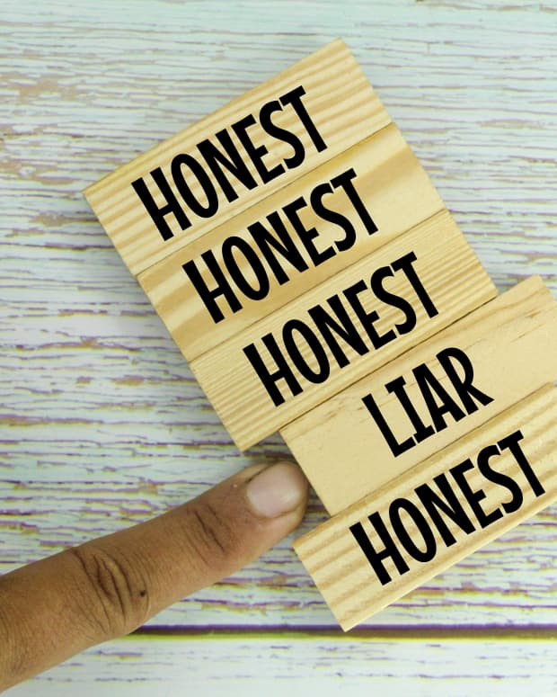 A close up on a row of tiny wooden blocks imprinted with the words "honest" and one imprinted with the word "liar". A finger is pointing to the one marked "liar", pushing it slightly out of position.