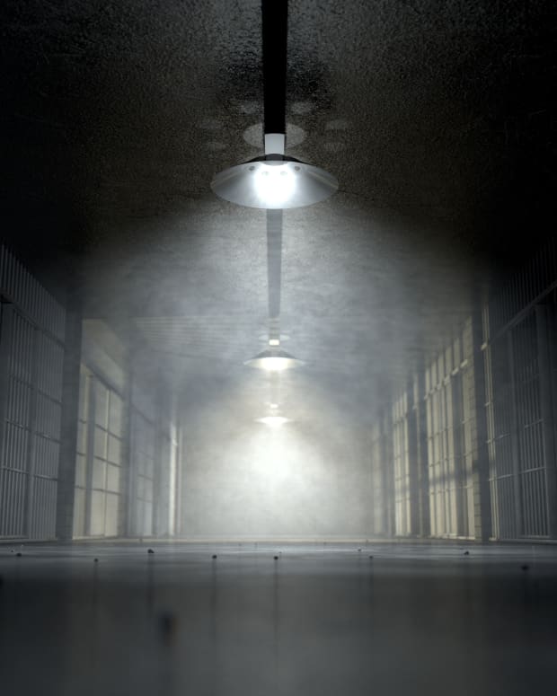 a prison hallway with jail cells on each side, lit by a ghostly overhead light.