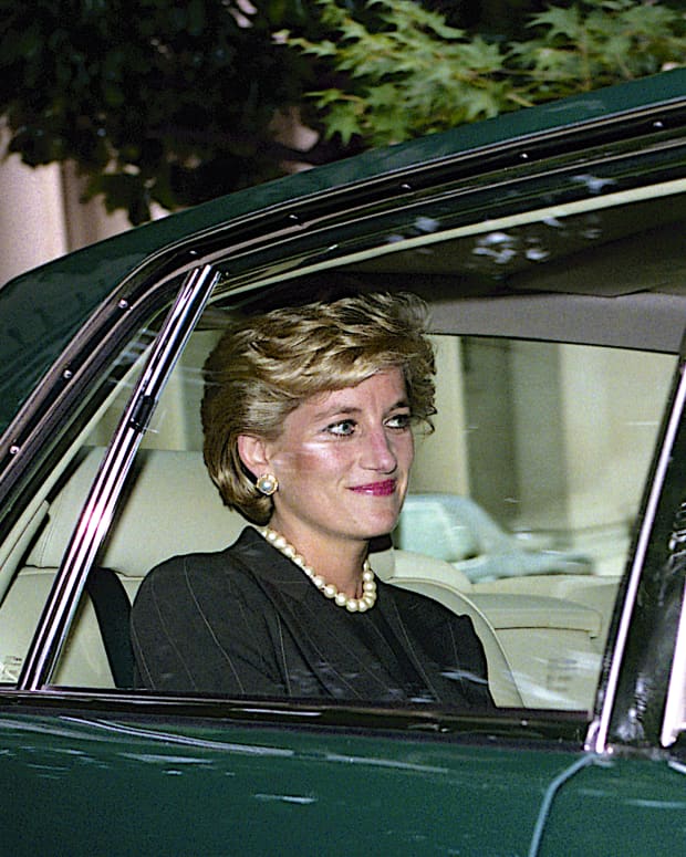 Princess Diana sits int he back seat of a green car, smiling.
