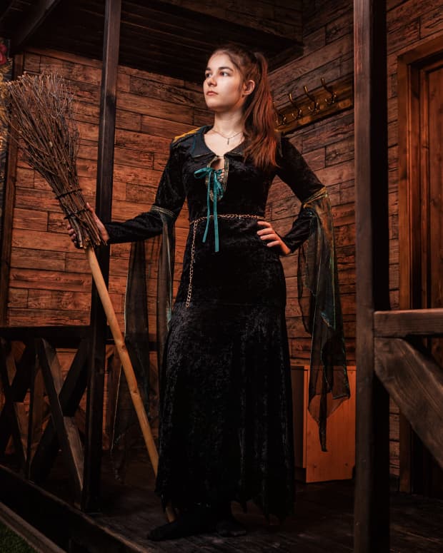 witch stands on the porch of her mysterious house with a broom in her hand