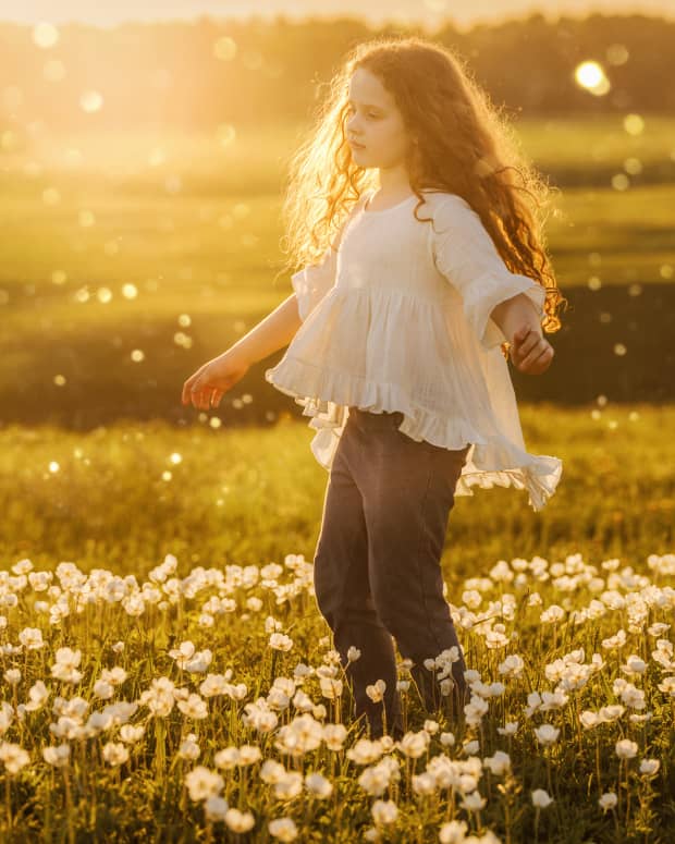 a little white girl with long curly brown hair stands in a field surrounded by ethereal light.