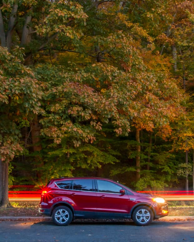 a red Ford EscapeSUV drives on a tree lined road