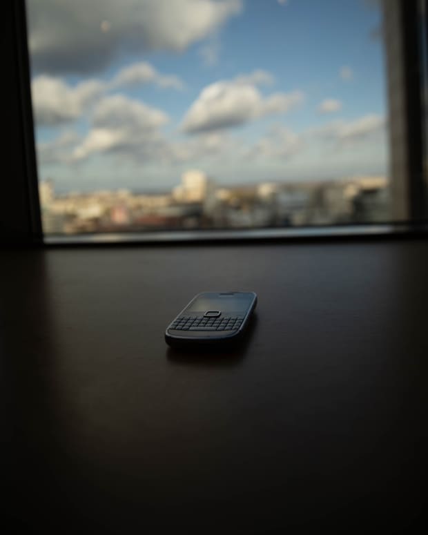an old cell phone lies ominously on a table in front of a large window