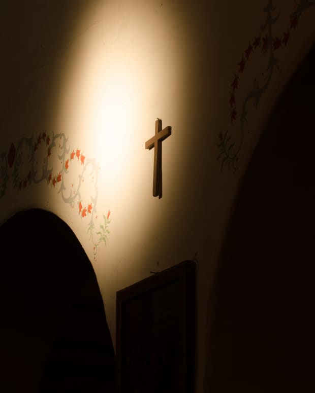 a cross hanging on a wall between two arches with a dramatic light shining on it.