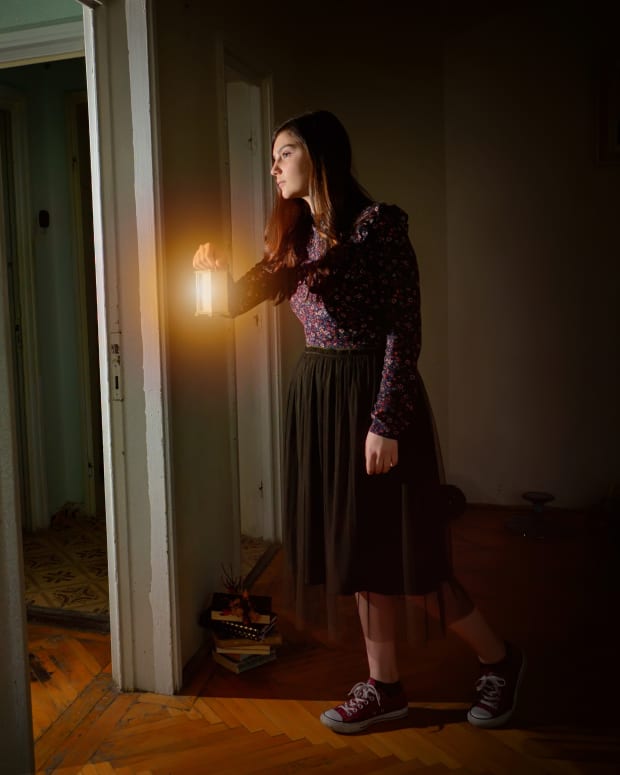 A woman holding a light peeks tentatively inside a door
