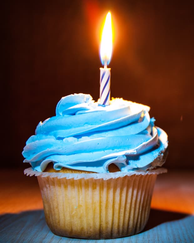 a lit candle on a blue cupcake against a dark background